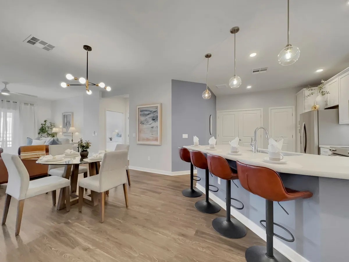 An open-concept kitchen and dining space, featuring a kitchen island with bar stools, modern decorative lighting, and a dining table set for a meal. Artwork and stylish accents add to the welcoming, contemporary feel.