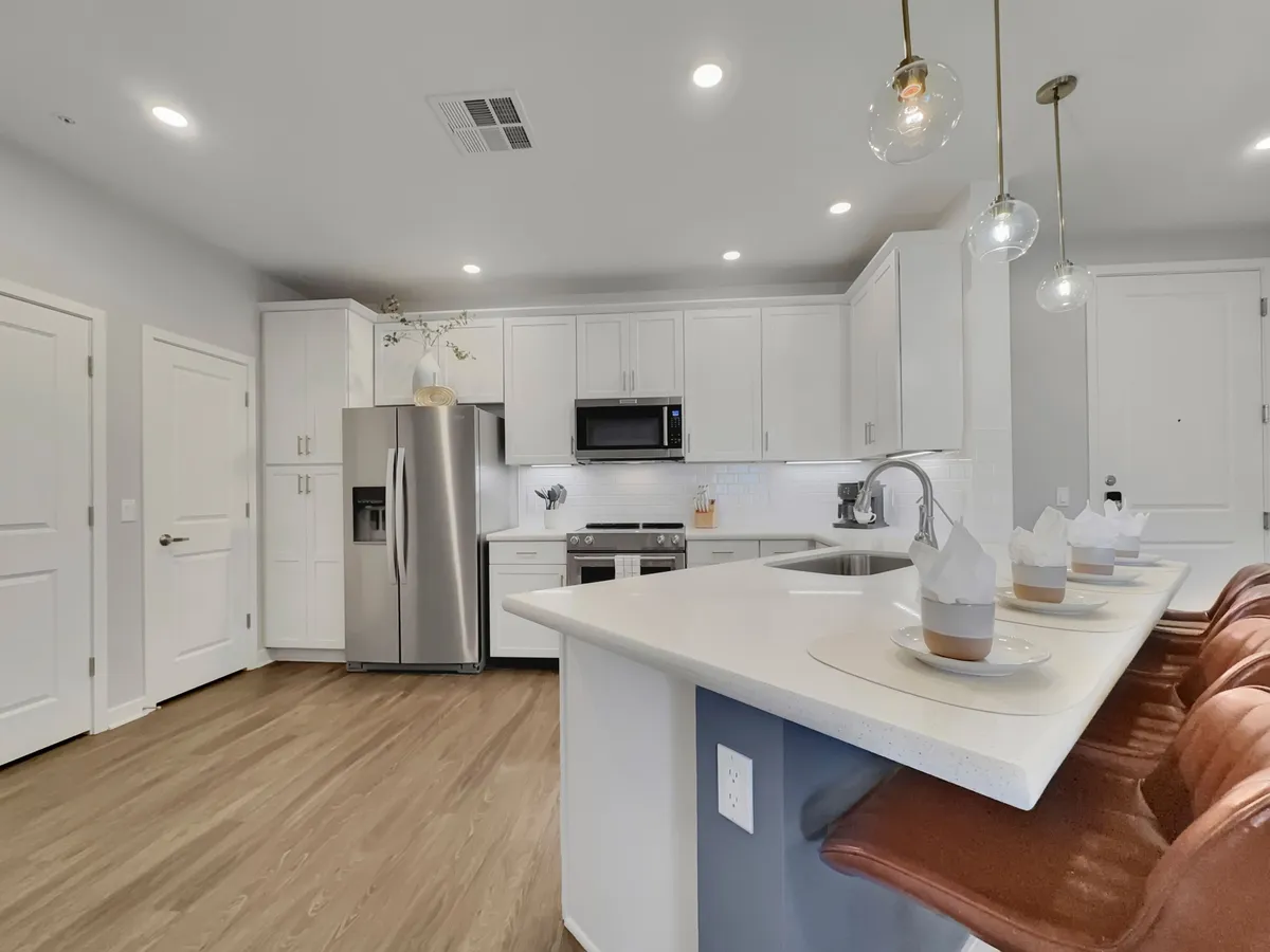 A bright, spacious kitchen with a central island, stainless steel appliances, white cabinetry, and pendant lighting. The layout is open, ideal for cooking, entertaining, and gathering with friends or family.