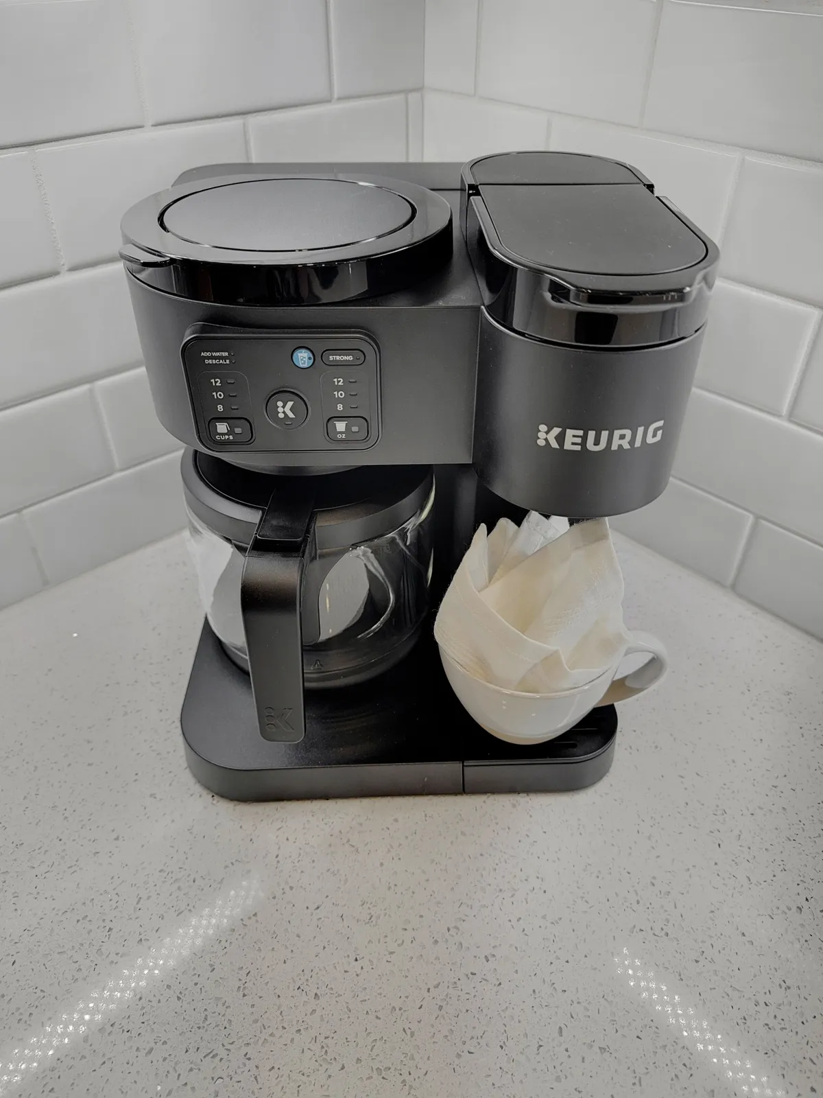 A close-up of the kitchen coffee station, complete with a Keurig coffee maker, glass coffee pot, and a white cup with coffee filters. The scene evokes a sense of morning rituals and the pleasure of sharing fresh coffee with loved ones.