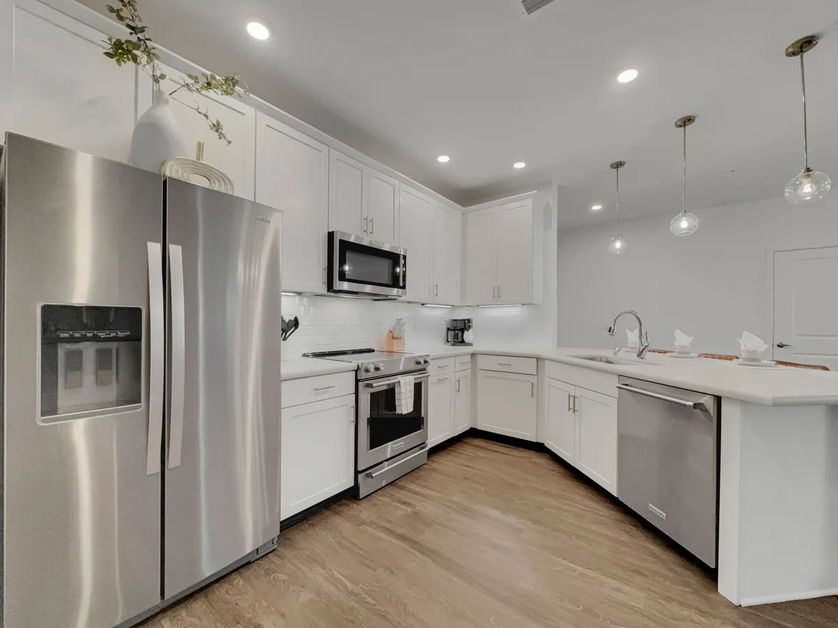 A bright, modern kitchen featuring a stainless steel refrigerator and stove, complemented by sleek white cabinets and a spacious kitchen island with a built-in sink. The inviting layout encourages both cooking and socializing, with room for guests or family to gather.
