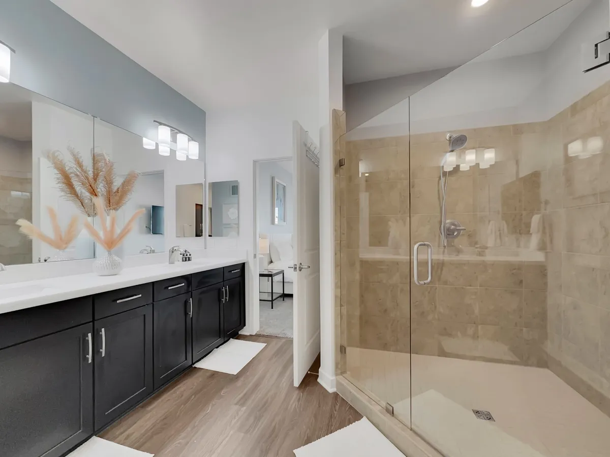 A spa-inspired bathroom with dual sinks, elegant fixtures, a large walk-in shower, and a decorative plant arrangement, radiating a serene and modern ambiance.