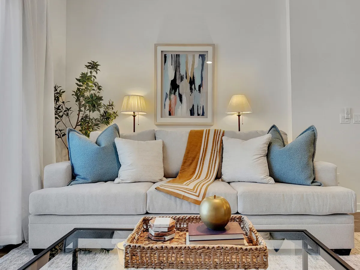 A cozy interior living room with a sofa, eye-catching artwork, decorative table pieces, lamps, and vibrant plants. The arrangement communicates a space ideal for relaxing after activities or hosting friends for conversation and connection.