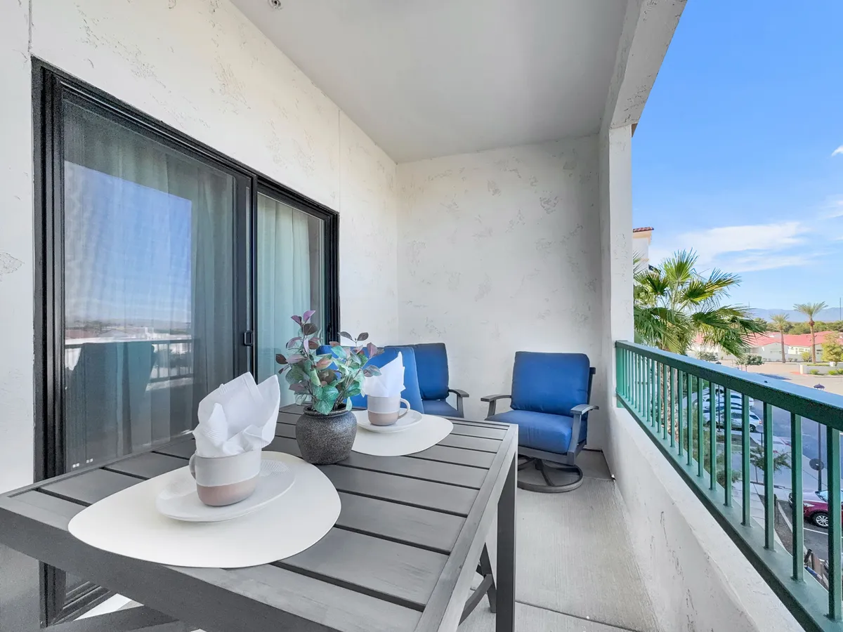 An inviting outdoor table setting with two blue chairs and a potted plant, overlooking a peaceful exterior area. The scene exudes a tranquil and welcoming mood, perfect for enjoying coffee, reading, or hosting a relaxed gathering.