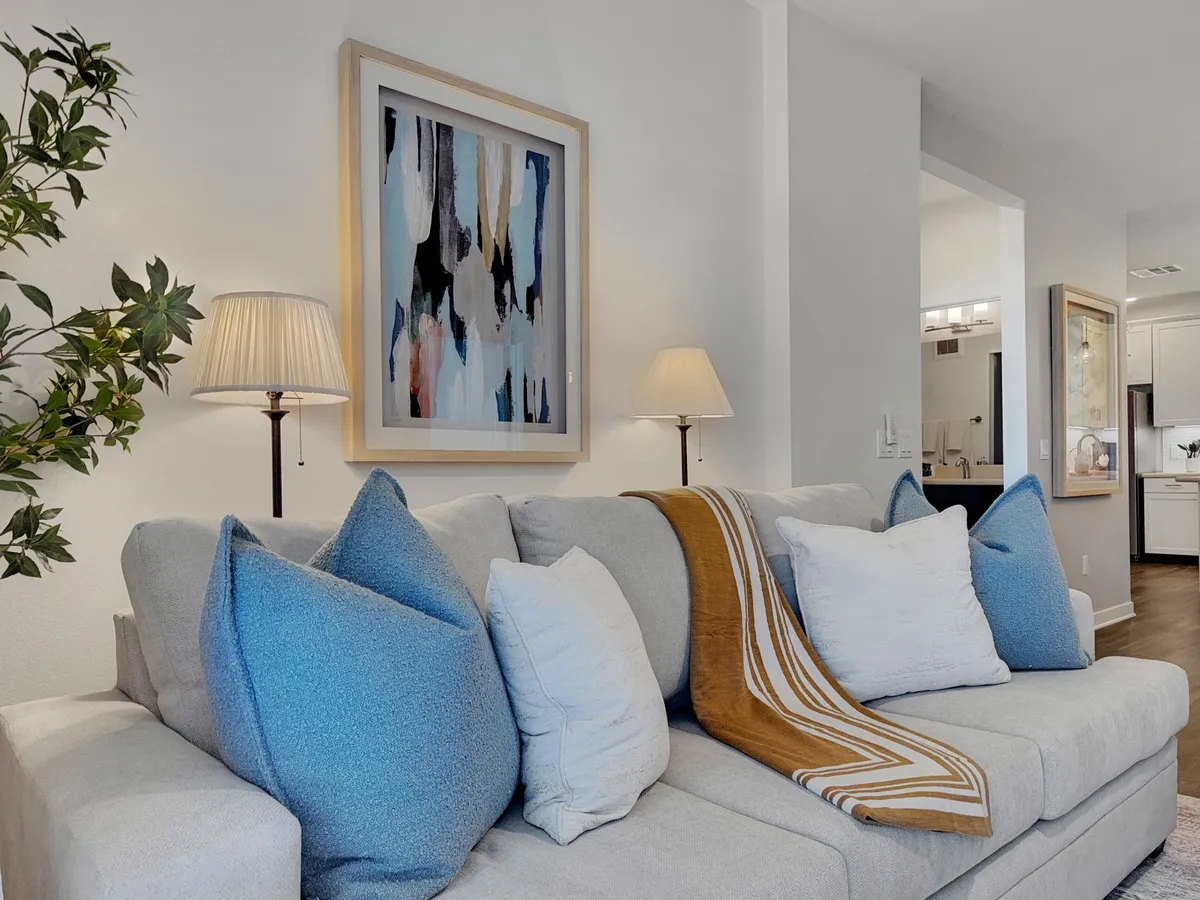 A cozy, open-concept living area featuring a comfortable sofa, stylish artwork, table lamps, and a soft throw blanket. The space is arranged for entertaining or relaxing, with a layout that encourages social interaction, movie nights, or casual gatherings with friends.