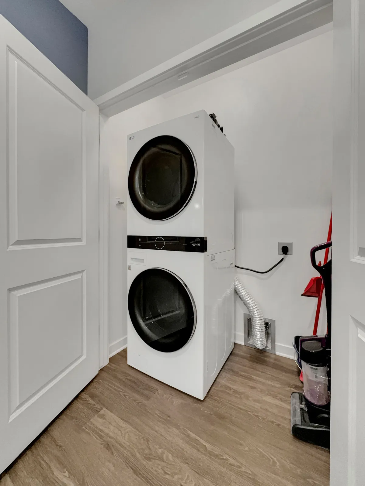 A compact laundry room featuring a stacked washer and dryer alongside cleaning supplies, designed for everyday convenience and efficient use of space.