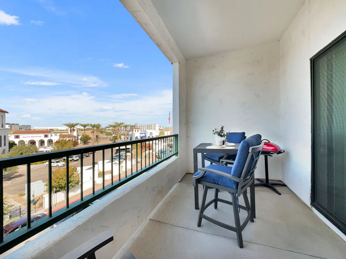 A calm balcony space furnished with comfortable outdoor seating and potted plants, with views of the street below. The mood is peaceful, suggesting a retreat for enjoying the breeze, reading, or people-watching.