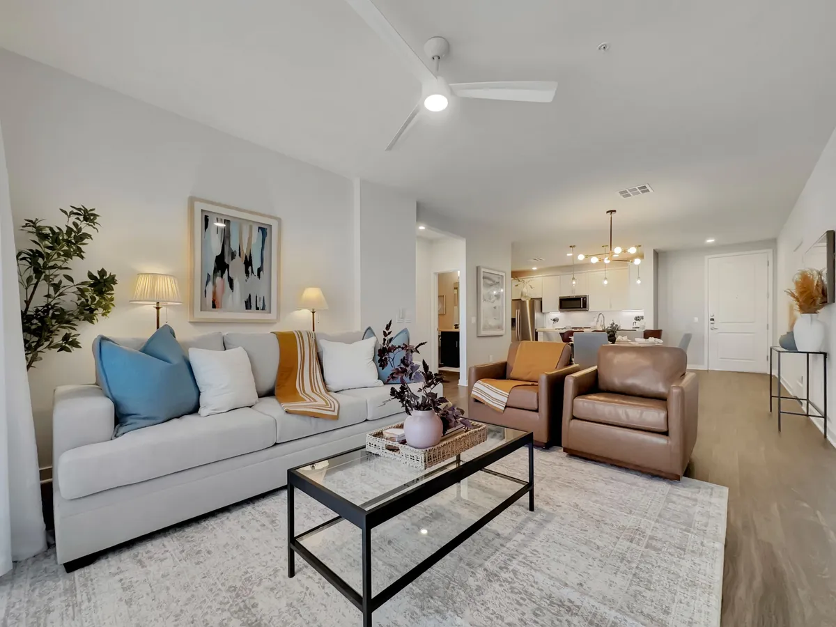 A contemporary living room featuring a plush, comfortable sofa with decorative pillows, a stylish armchair, a modern coffee table adorned with decor items, tasteful artwork on the wall, and a leafy indoor plant. Natural light fills the space, creating a cozy and welcoming atmosphere ideal for relaxation or hosting guests.
